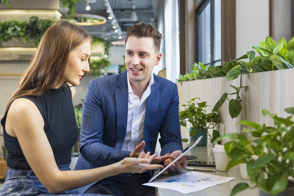 Geschäftsleute arbeiten an einer neuen Strategieplanung für das nächste Jahr – mit dem Laptop in einem umweltfreundlichen, modernen Arbeitsbereich in einem „Green Building“, umgeben von luftreinigenden Zimmerpflanzen.