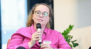 Frau in pinker Bluse spricht bei einer Veranstaltung in ein Mikrofon