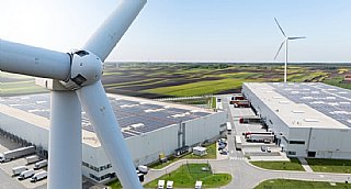 Windkraftanlagen vor einem Industriegebäude mit großflächigen Photovoltaikanlagen auf den Dächern