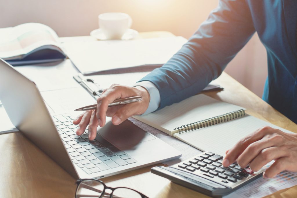 Geschäftsmann bei der Arbeit im Büro mit Taschenrechner und Laptop. Konzept: Finanzen und Buchhaltung