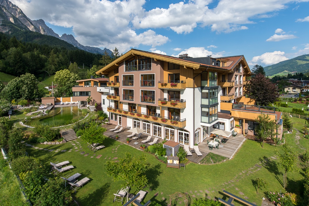 Hotelgebäude mit Gartenanlage vor alpiner Bergkulisse