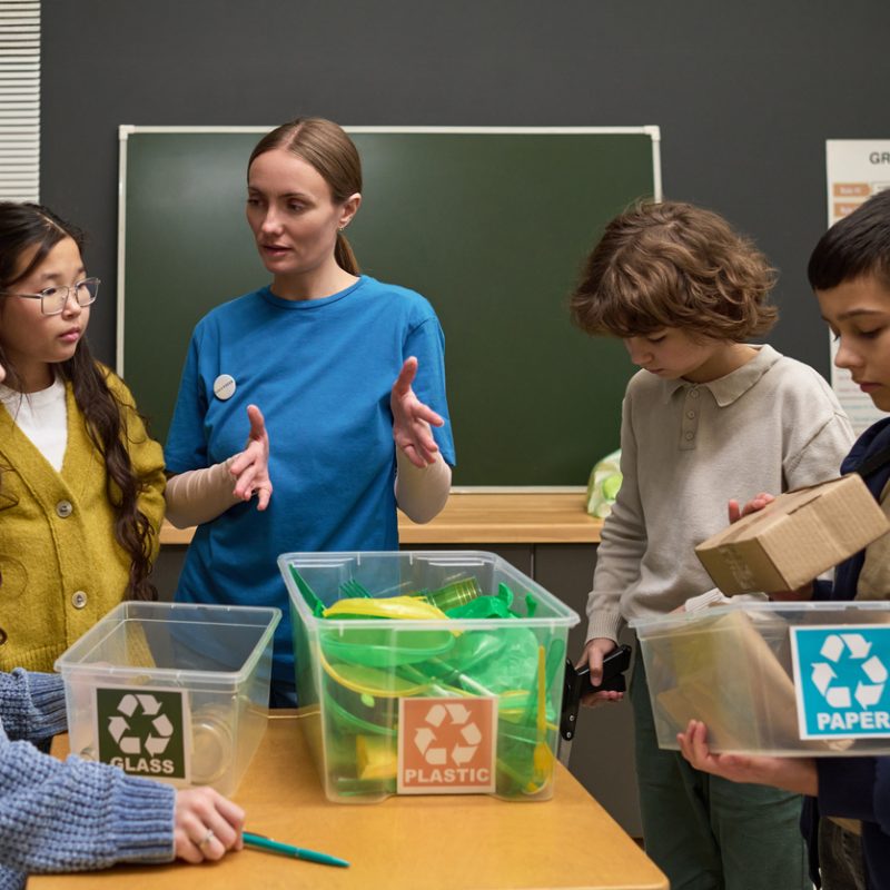 Frau, die Kinder beim Sortieren von Wertstoffen unterrichtet