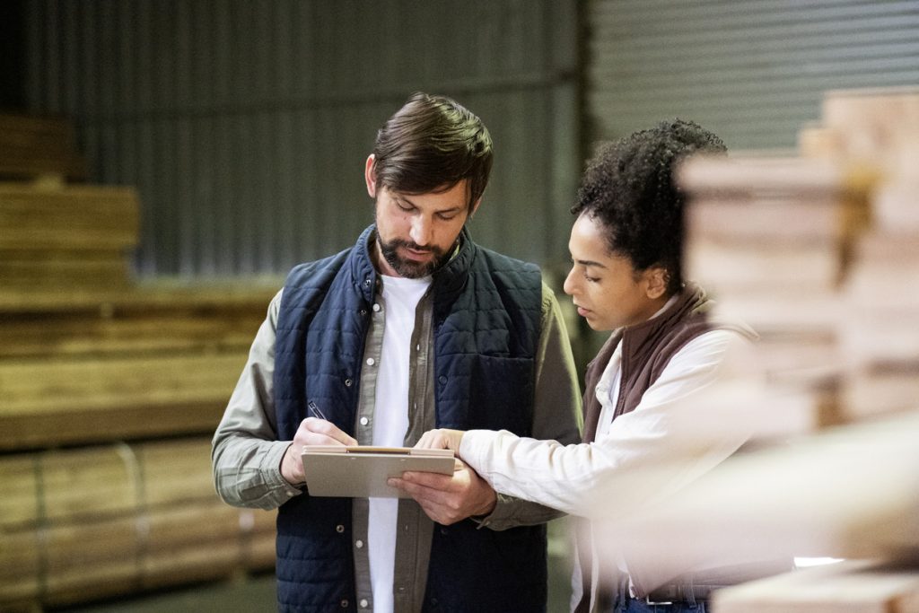 Besprechung, Bauarbeiten und Personen mit Klemmbrett im Lager zur Überprüfung, Checkliste und Bestandsaufnahme. Lagerung, Teamarbeit und ein Mann mit einer Frau mit Unterlagen für Baumaterial, Fertigung und Planung